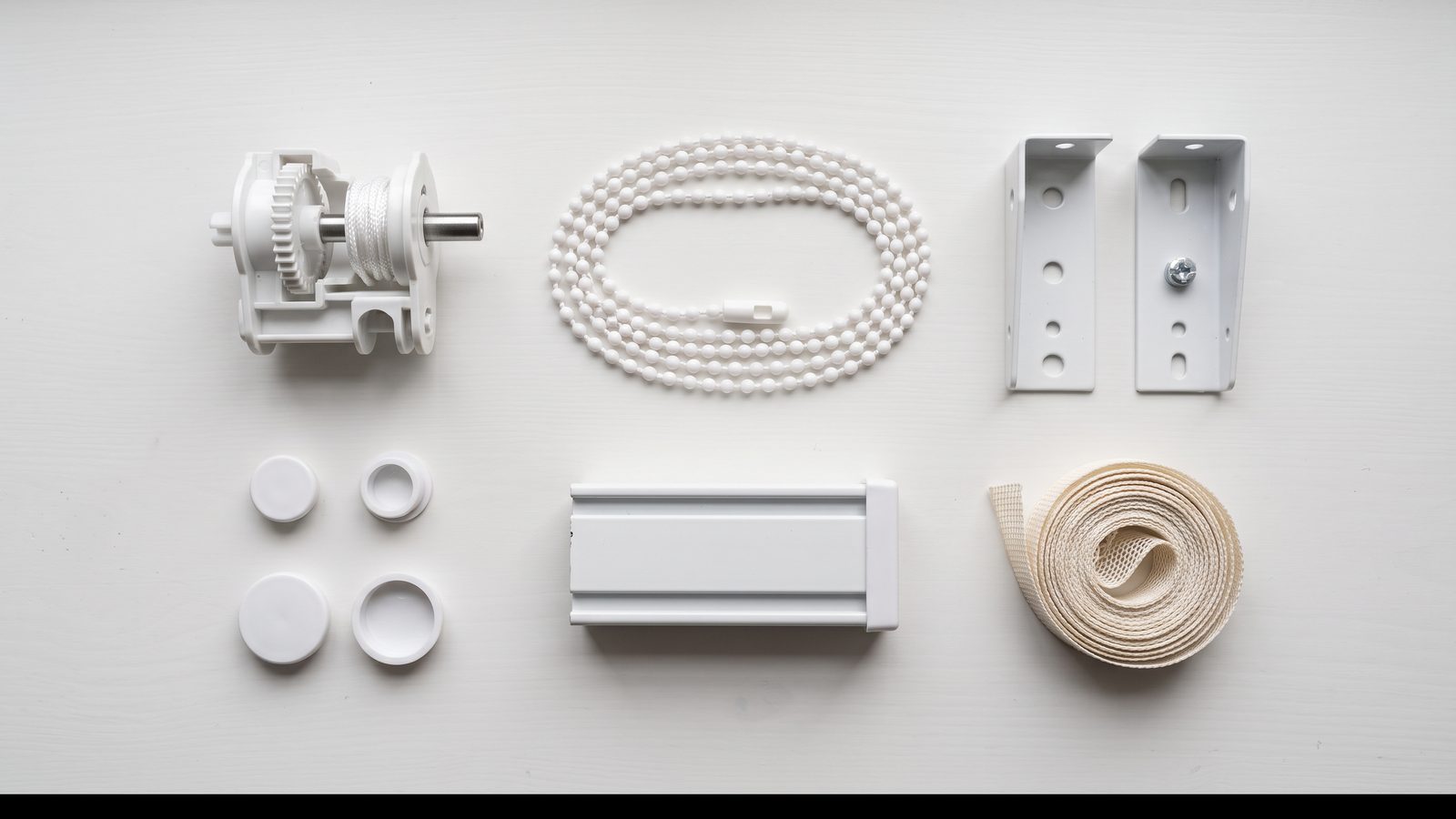 Roller and venetian blind spare parts laid out — clutch, chain, brackets, end caps and ladder tape