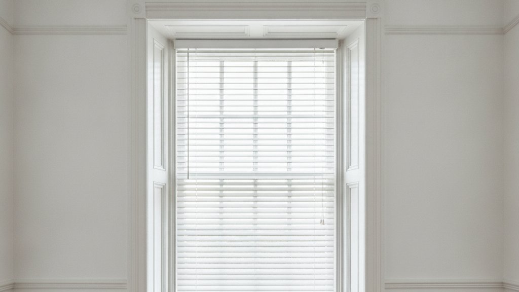 White venetian blind with narrow slats fitted to a tall Victorian sash window in a period room